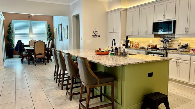 kitchen featuring backsplash, a kitchen island with sink, sink, light stone counters, and a breakfast bar area