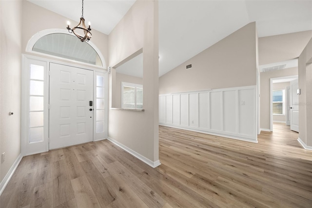 foyer with a wealth of natural light, light hardwood / wood-style flooring, high vaulted ceiling, and a notable chandelier