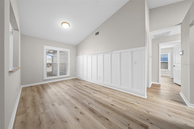 spare room with a healthy amount of sunlight, light wood-type flooring, and vaulted ceiling