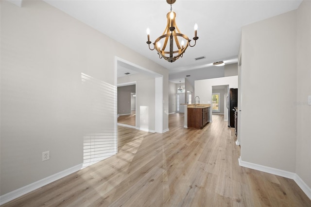 unfurnished dining area with light wood-type flooring, sink, and an inviting chandelier