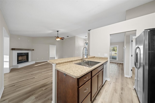 kitchen with light stone countertops, light wood-type flooring, stainless steel appliances, ceiling fan, and sink