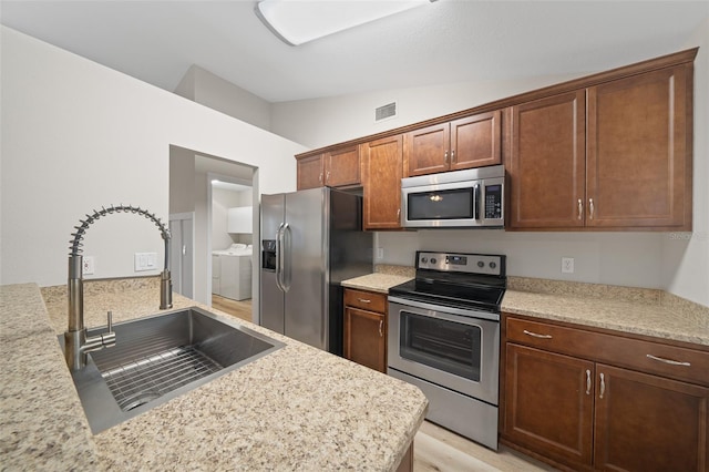 kitchen with light stone countertops, sink, washing machine and dryer, vaulted ceiling, and appliances with stainless steel finishes