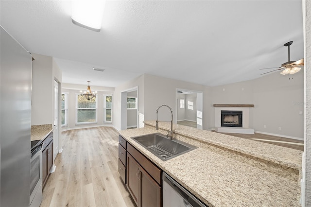 kitchen with pendant lighting, sink, light hardwood / wood-style flooring, light stone countertops, and stainless steel appliances