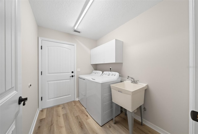 clothes washing area with cabinets, sink, light hardwood / wood-style flooring, washing machine and dryer, and a textured ceiling