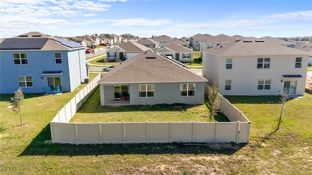 rear view of house featuring a residential view, roof mounted solar panels, a fenced backyard, and a lawn