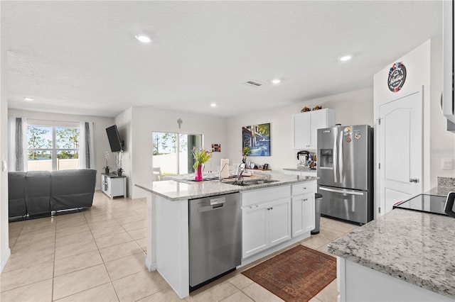 kitchen featuring light stone counters, stainless steel appliances, white cabinets, a kitchen island with sink, and a sink