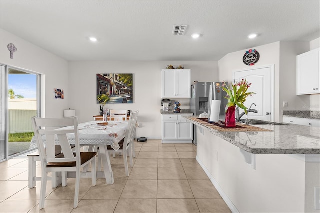 kitchen with a center island with sink, visible vents, light stone counters, white cabinetry, and a sink