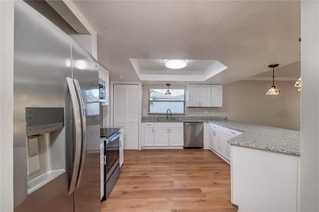 kitchen with appliances with stainless steel finishes, light wood-type flooring, a tray ceiling, pendant lighting, and white cabinetry