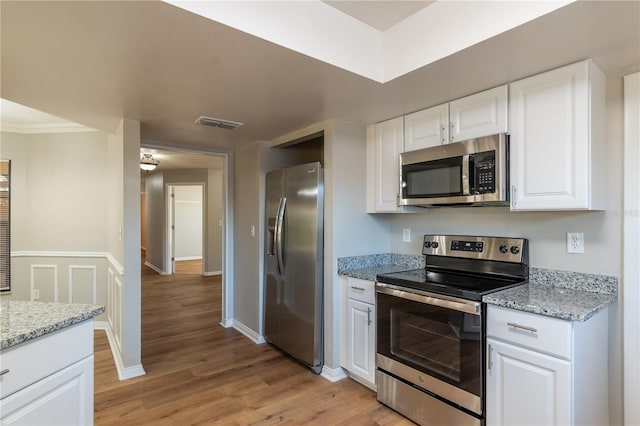 kitchen with light stone counters, white cabinetry, stainless steel appliances, and light hardwood / wood-style flooring