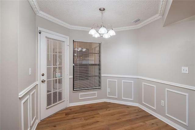 unfurnished dining area featuring crown molding, hardwood / wood-style floors, a textured ceiling, and an inviting chandelier