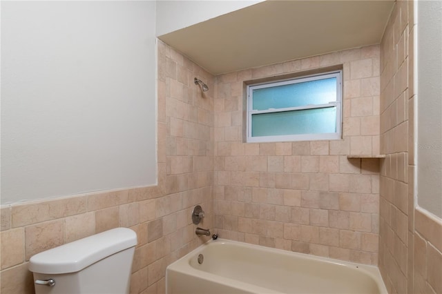 bathroom with tiled shower / bath combo, toilet, and tile walls