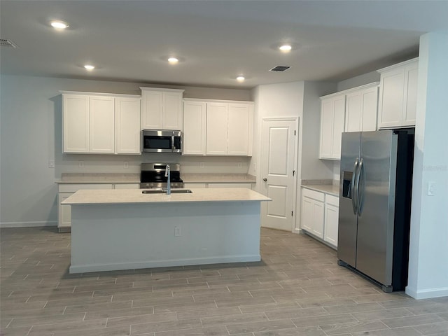 kitchen with an island with sink, sink, white cabinets, and stainless steel appliances