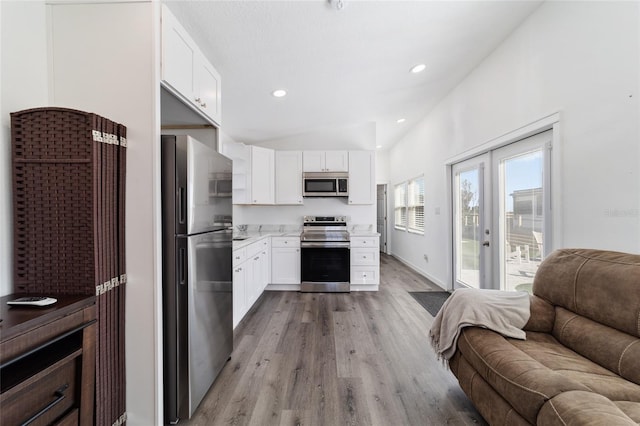 kitchen with white cabinets, light wood-type flooring, vaulted ceiling, and appliances with stainless steel finishes