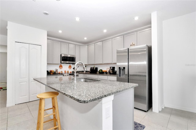 kitchen featuring sink, gray cabinets, an island with sink, appliances with stainless steel finishes, and light stone counters