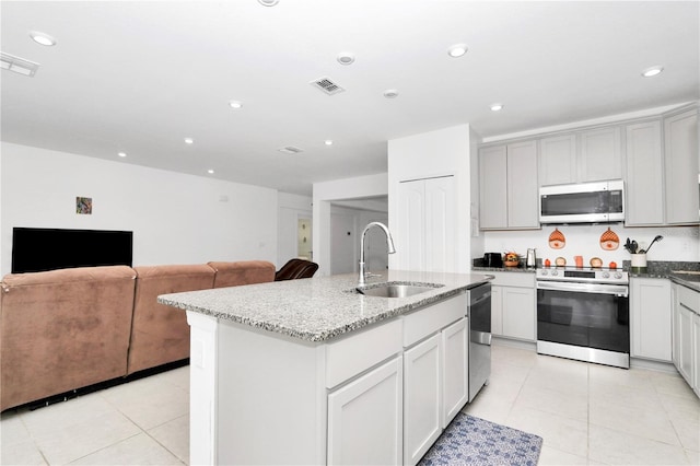 kitchen featuring appliances with stainless steel finishes, light stone counters, sink, light tile patterned floors, and a center island with sink