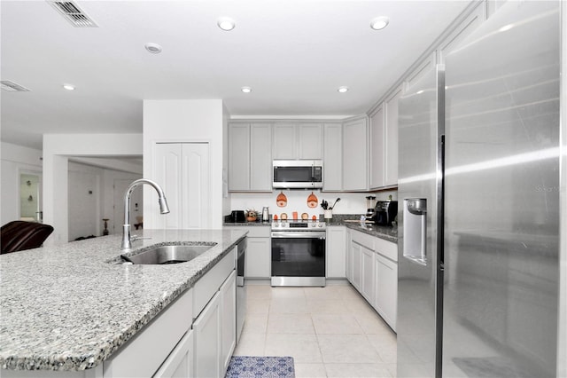 kitchen featuring a center island with sink, sink, light stone countertops, appliances with stainless steel finishes, and light tile patterned flooring