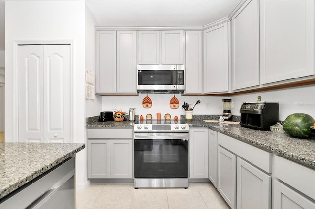 kitchen featuring gray cabinets, light stone counters, light tile patterned floors, and appliances with stainless steel finishes