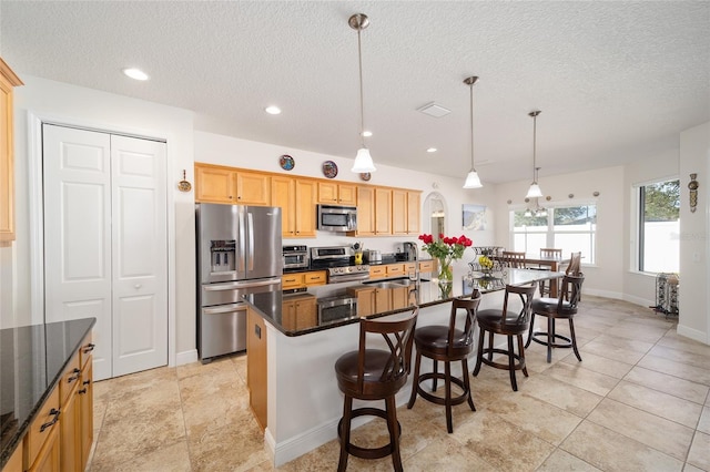 kitchen featuring pendant lighting, a textured ceiling, stainless steel appliances, and an island with sink