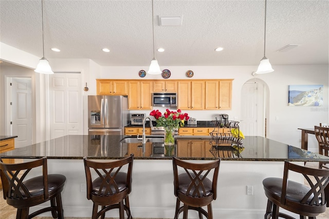 kitchen with a textured ceiling, a spacious island, hanging light fixtures, and appliances with stainless steel finishes