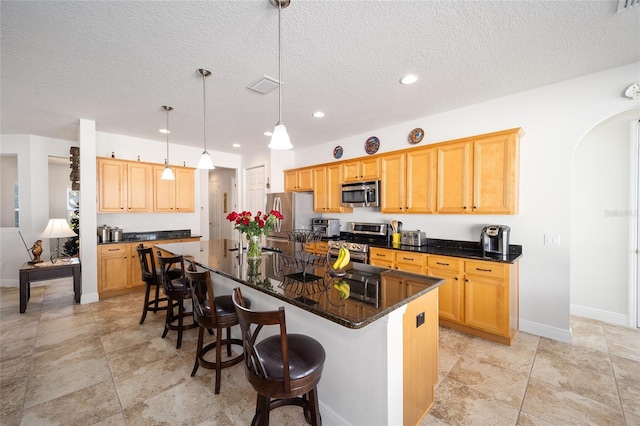 kitchen featuring appliances with stainless steel finishes, a textured ceiling, decorative light fixtures, and a kitchen island with sink