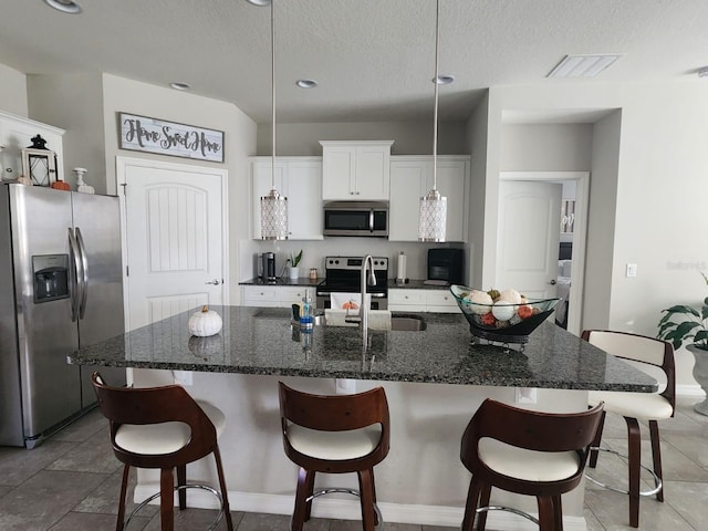 kitchen featuring white cabinets, sink, dark stone countertops, an island with sink, and stainless steel appliances