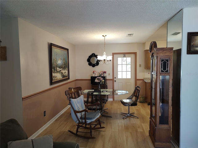 dining room with a textured ceiling, light wood-type flooring, and a notable chandelier