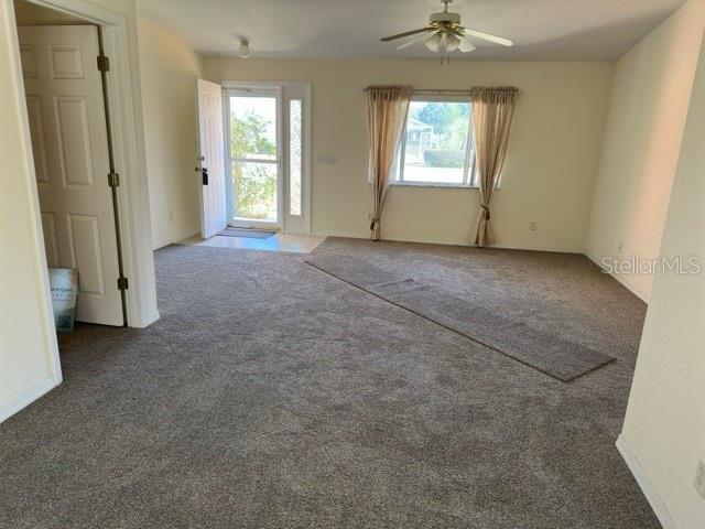 empty room with ceiling fan, a healthy amount of sunlight, and dark carpet