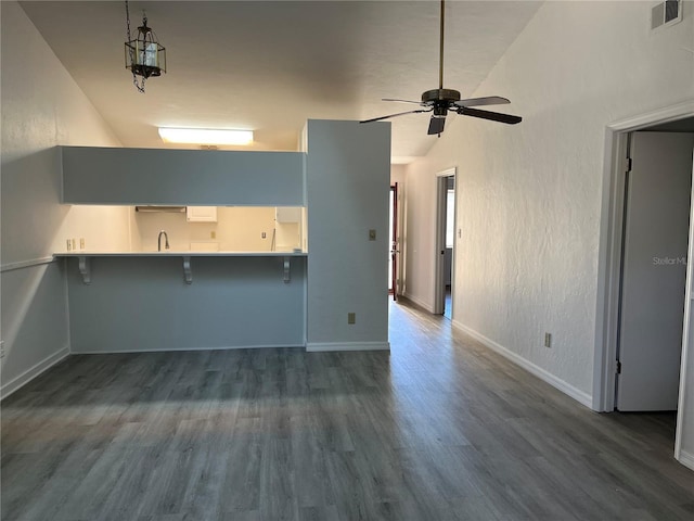 kitchen with a kitchen breakfast bar, kitchen peninsula, dark wood-type flooring, and high vaulted ceiling