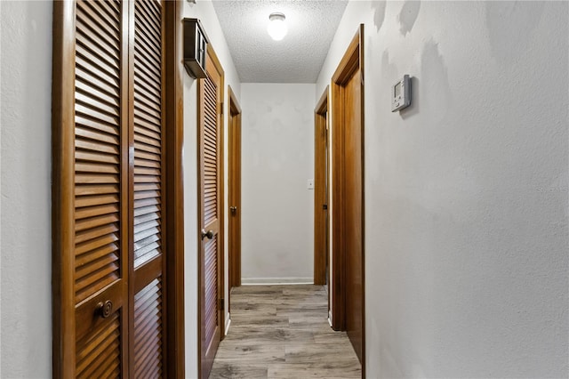 corridor with a textured ceiling and light wood-type flooring