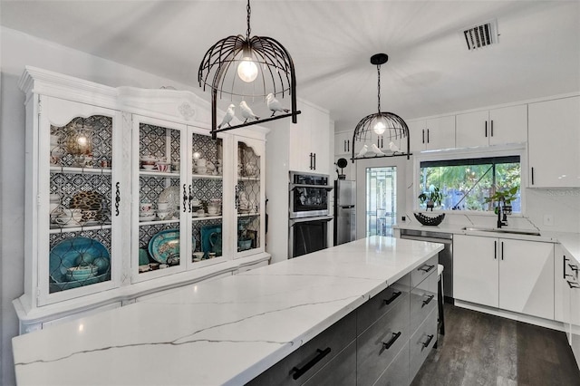 kitchen featuring visible vents, white cabinets, appliances with stainless steel finishes, decorative light fixtures, and a sink