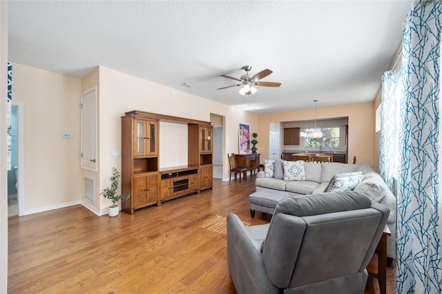 living room with ceiling fan, light wood-type flooring, and a textured ceiling