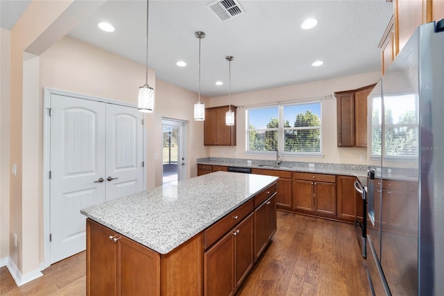 kitchen featuring a center island, stainless steel fridge, light stone countertops, decorative light fixtures, and wood-type flooring