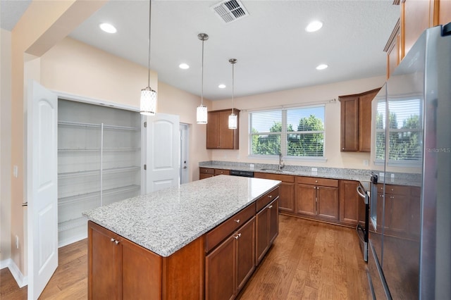 kitchen with stainless steel fridge, light wood-type flooring, sink, decorative light fixtures, and a kitchen island