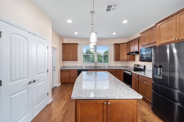 kitchen featuring hardwood / wood-style floors, black appliances, decorative light fixtures, a kitchen island, and light stone counters