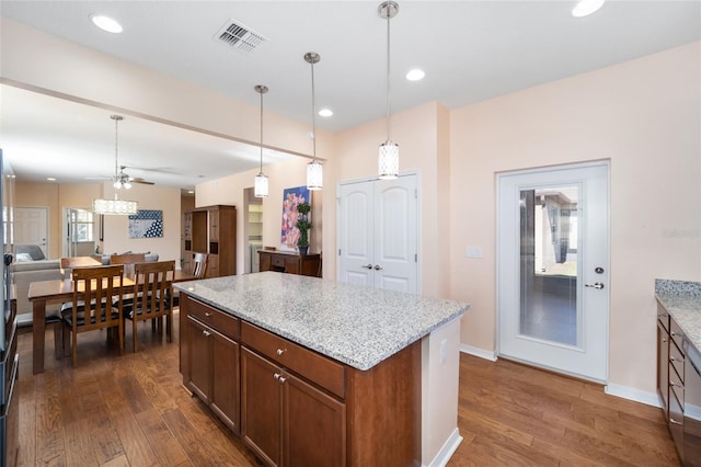 kitchen featuring ceiling fan, a center island, hanging light fixtures, light stone counters, and dark hardwood / wood-style flooring