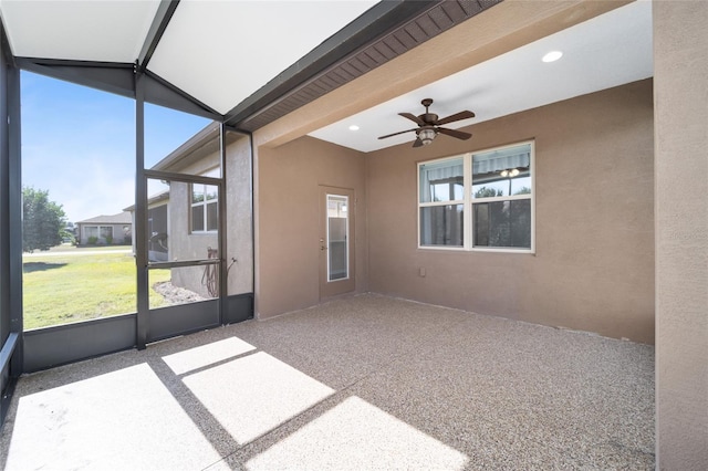 unfurnished sunroom featuring beamed ceiling, ceiling fan, and a healthy amount of sunlight