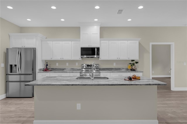 12205 SW 71st Lane Rd, Ocala, FL 34481 - kitchen with stainless steel appliances, white cabinetry, an island with sink, light wood-style floors, and light stone countertops