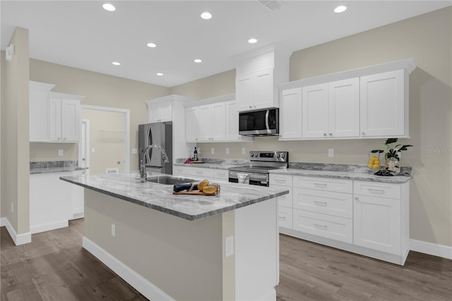 12205 SW 71st Lane Rd, Ocala, FL 34481 - kitchen with stainless steel appliances, wood finished floors, a center island with sink, white cabinets, and light stone countertops