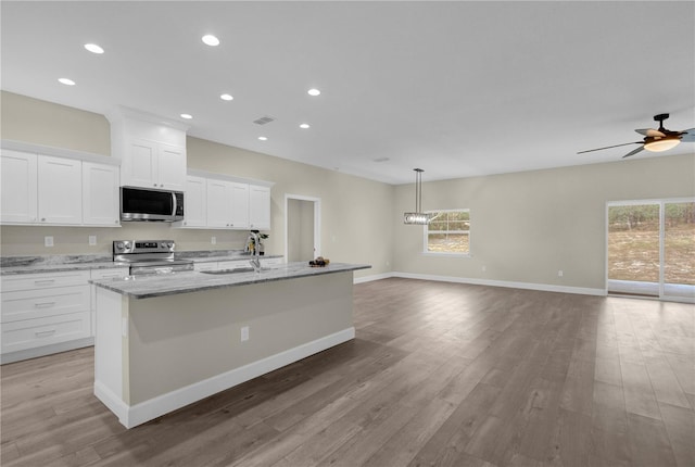 kitchen with white cabinets, a center island with sink, stainless steel appliances, and light hardwood / wood-style flooring