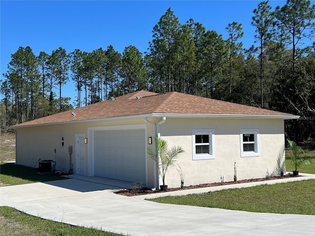 view of front of property with stucco siding, central AC unit, concrete driveway, and a shingled roof