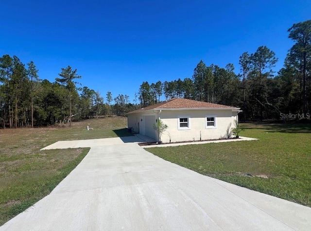 view of side of home featuring a yard, a garage, driveway, and stucco siding