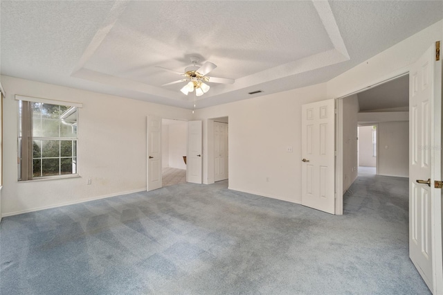 unfurnished bedroom with carpet, ceiling fan, a raised ceiling, and a textured ceiling