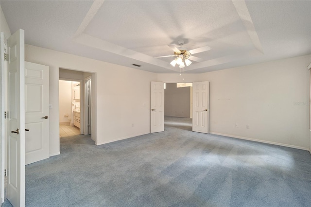 unfurnished bedroom featuring light carpet, a textured ceiling, a raised ceiling, ceiling fan, and connected bathroom