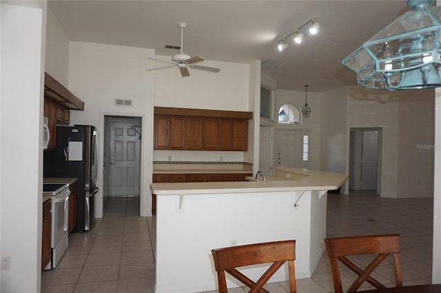 kitchen featuring white appliances, light tile patterned flooring, a high ceiling, and a kitchen bar