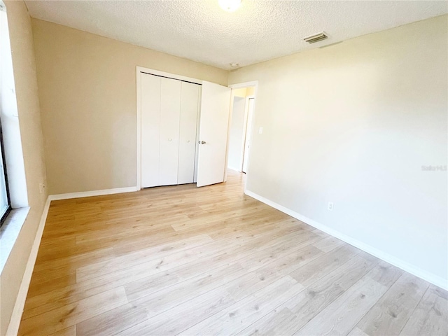 unfurnished bedroom with a textured ceiling, light hardwood / wood-style flooring, and a closet