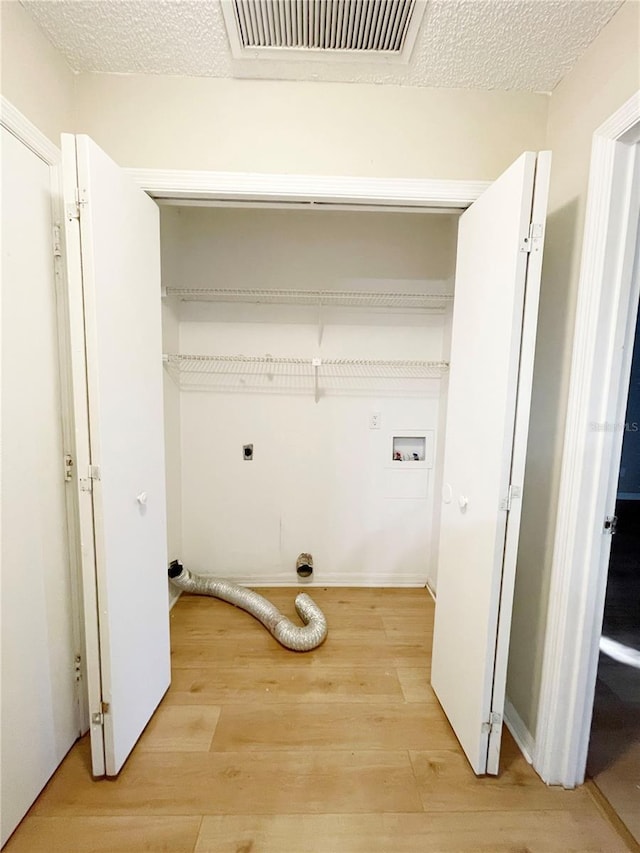 laundry room featuring hookup for an electric dryer, light hardwood / wood-style floors, a textured ceiling, and washer hookup