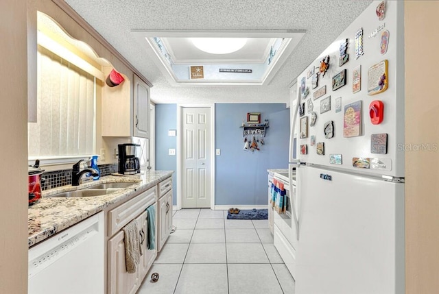 kitchen with white appliances, a raised ceiling, sink, light tile patterned floors, and a textured ceiling