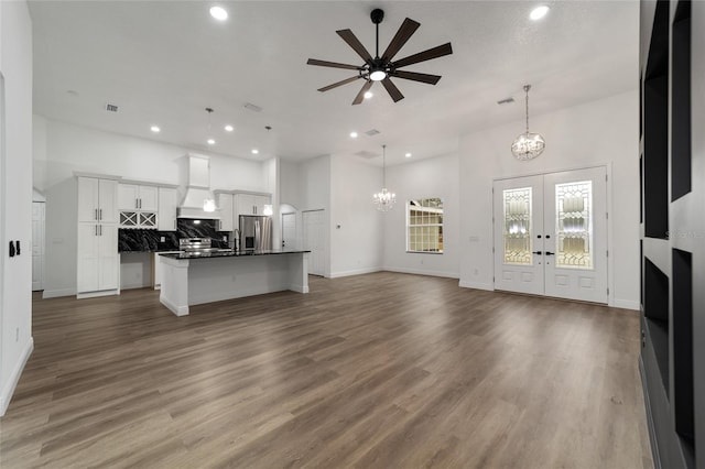 unfurnished living room with hardwood / wood-style floors, ceiling fan with notable chandelier, and french doors