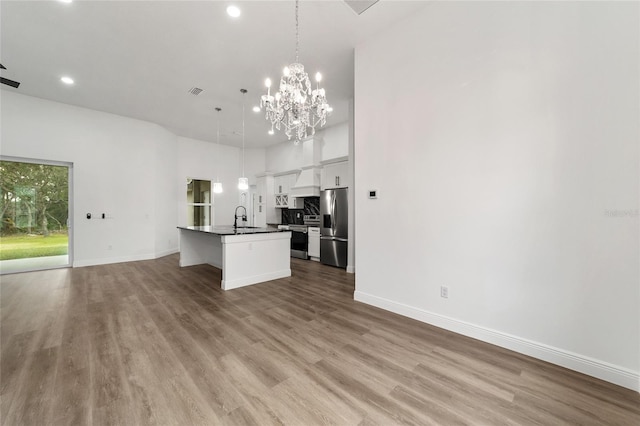 kitchen featuring appliances with stainless steel finishes, a kitchen island with sink, sink, decorative light fixtures, and white cabinetry