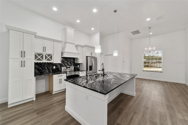 kitchen with dark wood-type flooring, a large island with sink, dark stone counters, custom range hood, and appliances with stainless steel finishes